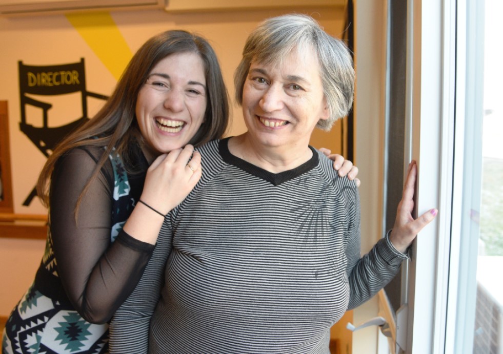 Cassandra and Karen Best, standing by a window inside and smiling.