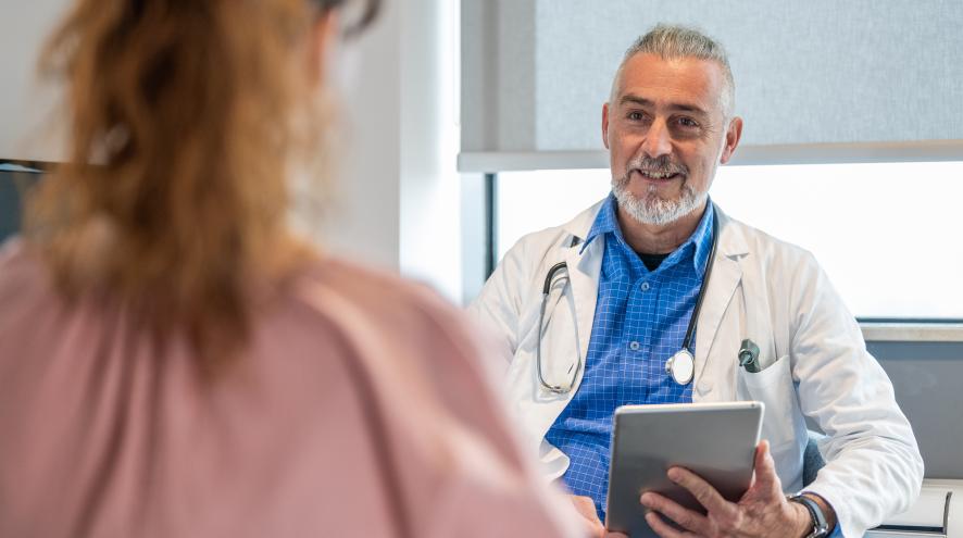 Male medical professional looking towards us while speaking to a woman in the foreground.