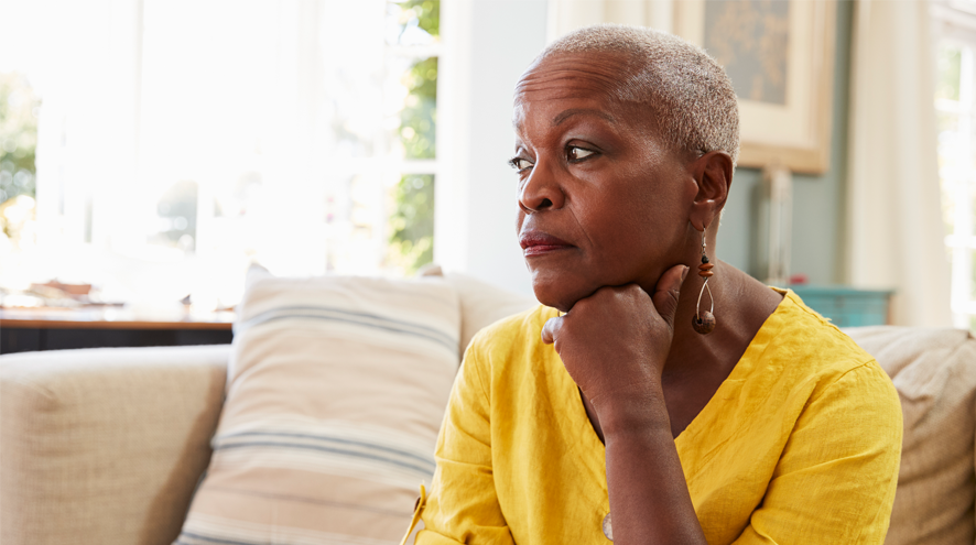 A midlife woman sits by a window looking serious and solemn, her hand under her chin