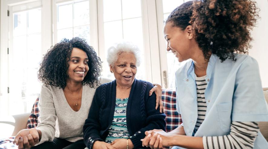 Younger woman with arm around older woman speak to caregiver