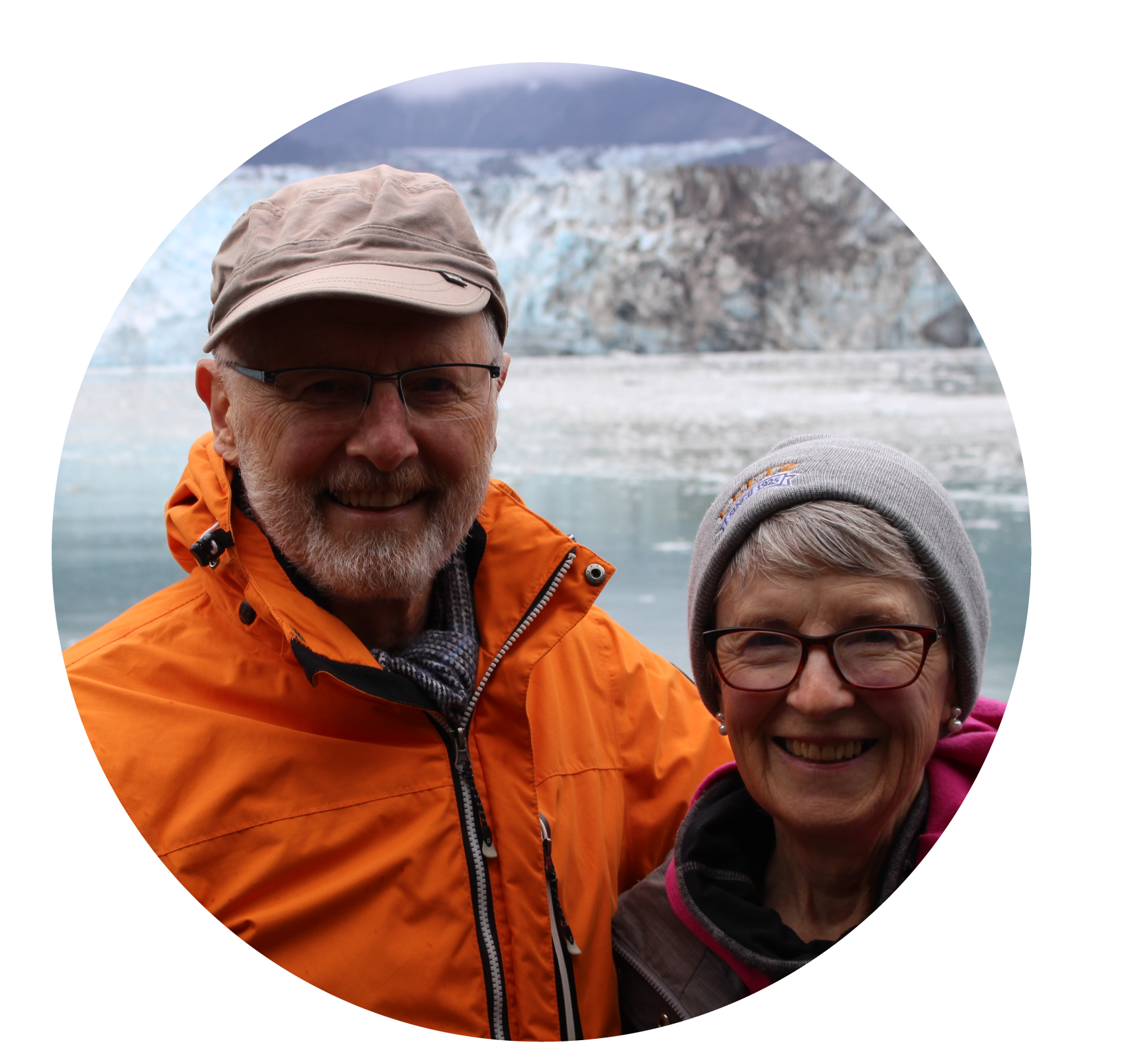 Man in bright orange jacket and tan hat with arm around woman in pink jacket and grey toque, both smiling