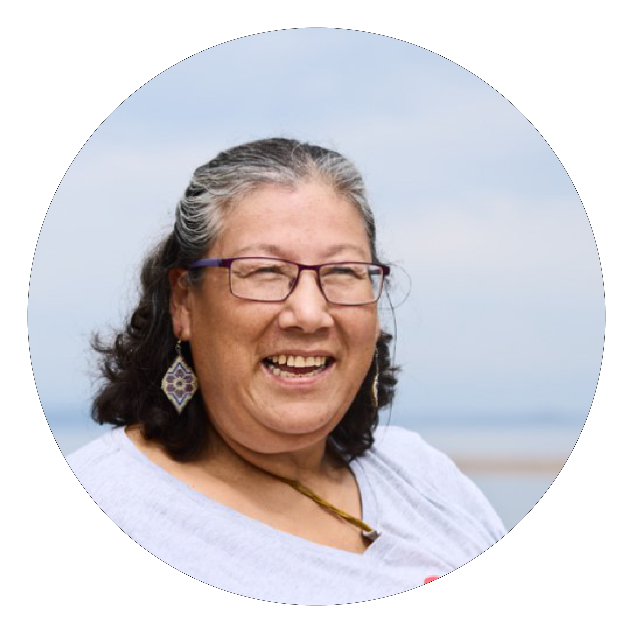 A woman with black and grey hair in a white shirt and glasses, smiling