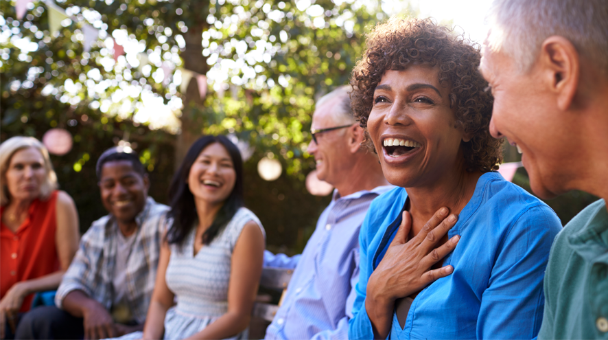 Six midlife people sit outdoors talking and laughing