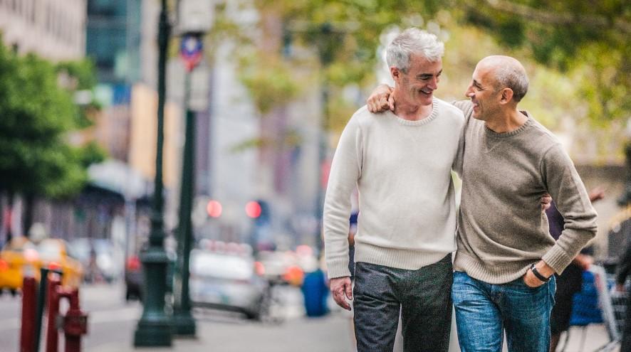 Two middle-aged men smiling happily and walking together down the street.