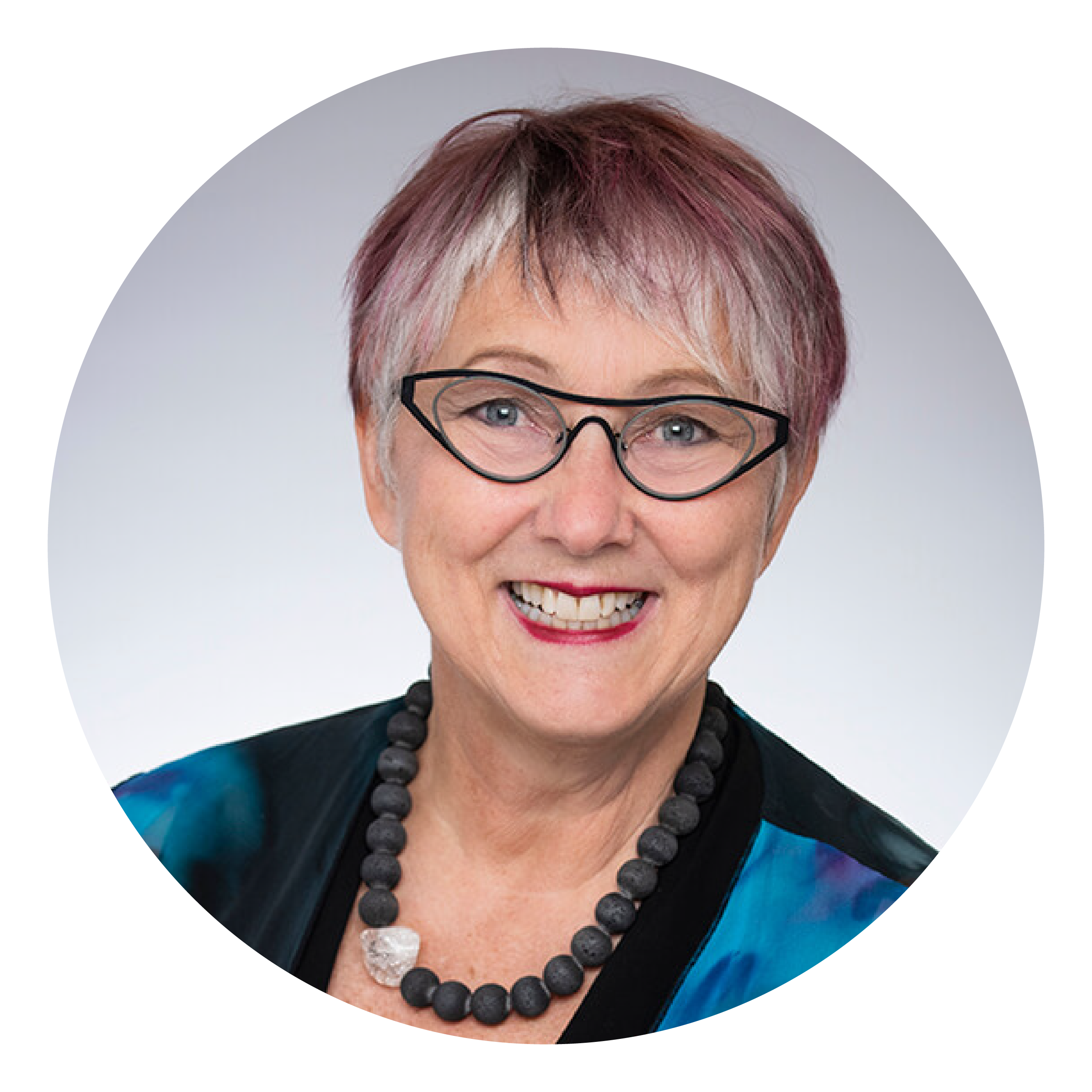 A smiling woman with short grey and purple hair and black glasses