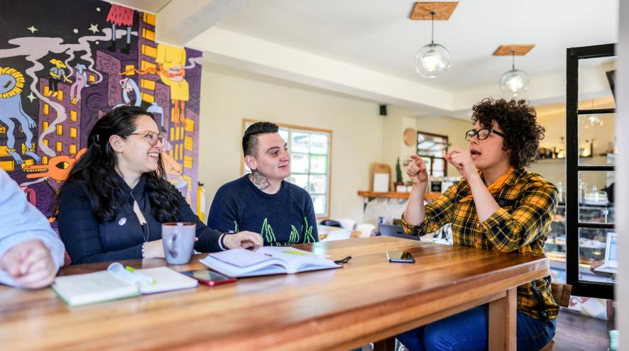 3 people sit at a cafe table; 1 is speaking, the other two are listening