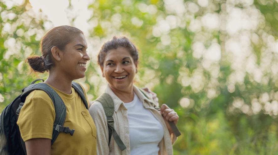 An older midlife woman and a younger woman with backpacks walking and talking in forest