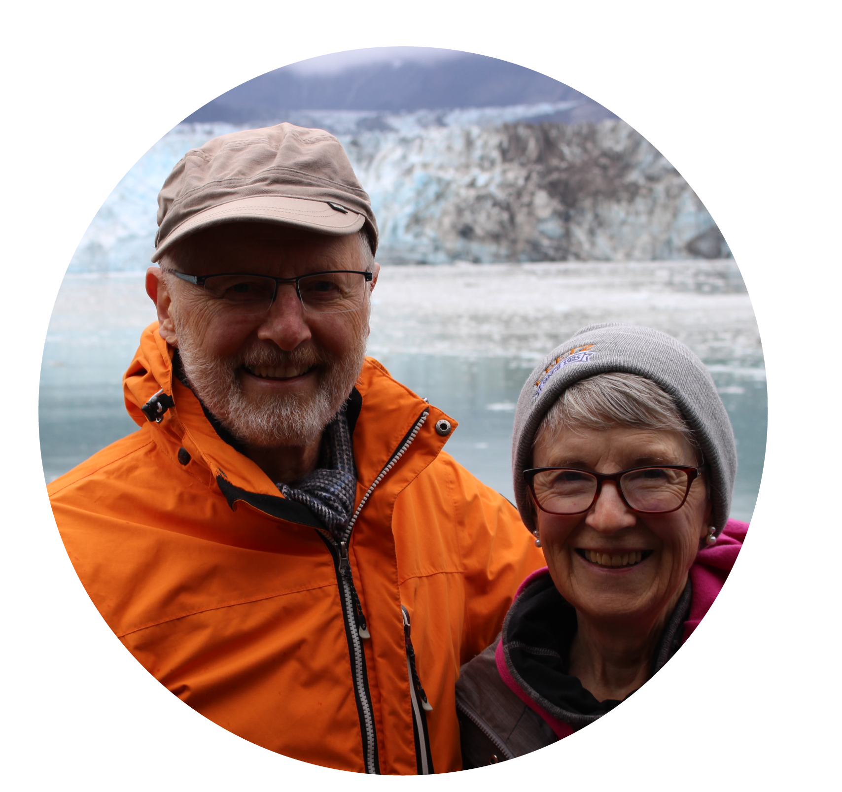 Man in bright orange jacket and tan hat with arm around woman in pink jacket and grey toque, both smiling