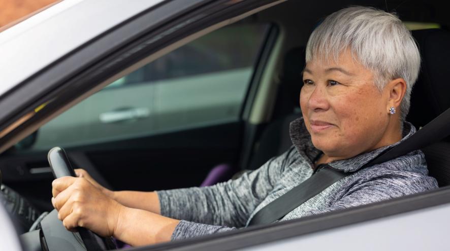 Older woman in stopped car with hands on wheel and seatbelt on