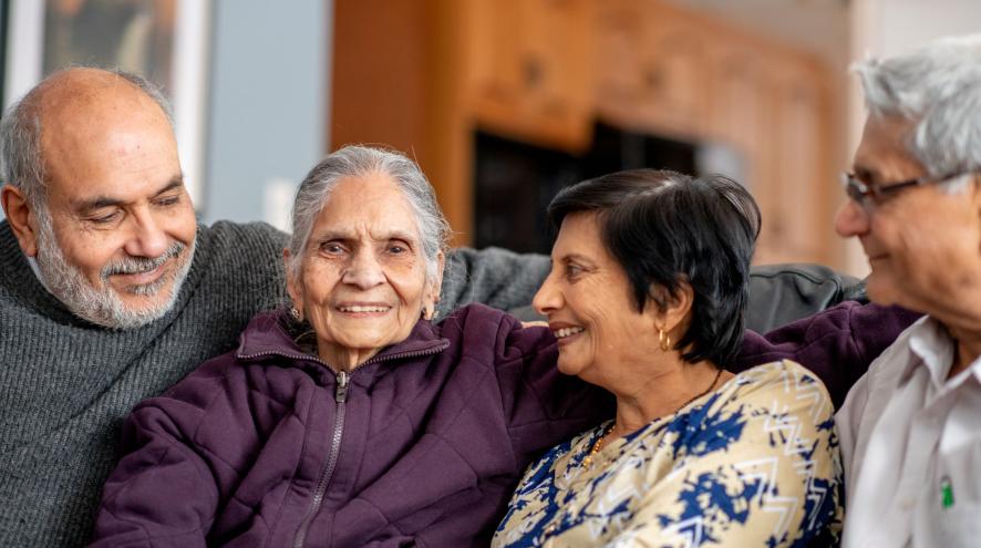 Two older women and two holder men sit on couch together, smiling