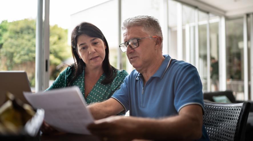 Two people look at a laptop and papers at home