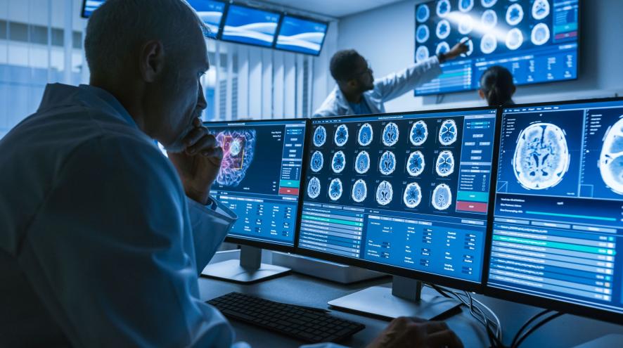 A  man looks at computer images of brain scans in foreground; a man and a woman look at more brain scans in background