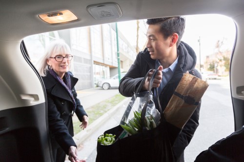 Young man helping a senior woman with taking the groceries out of the car.