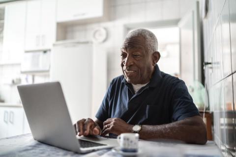 Older man sits with laptop at kitchen table