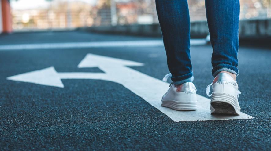 Legs and feet in jeans and sneakers walking on road direction