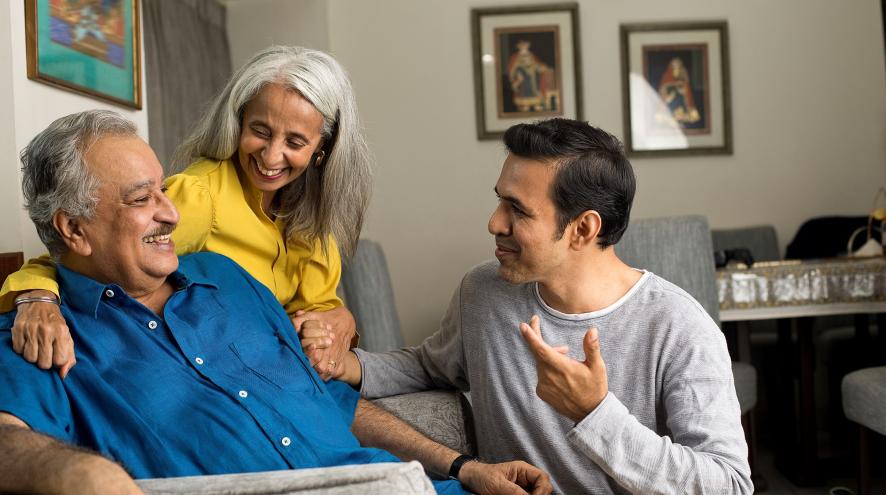 An older man, older woman and younger man are smiling and talking 