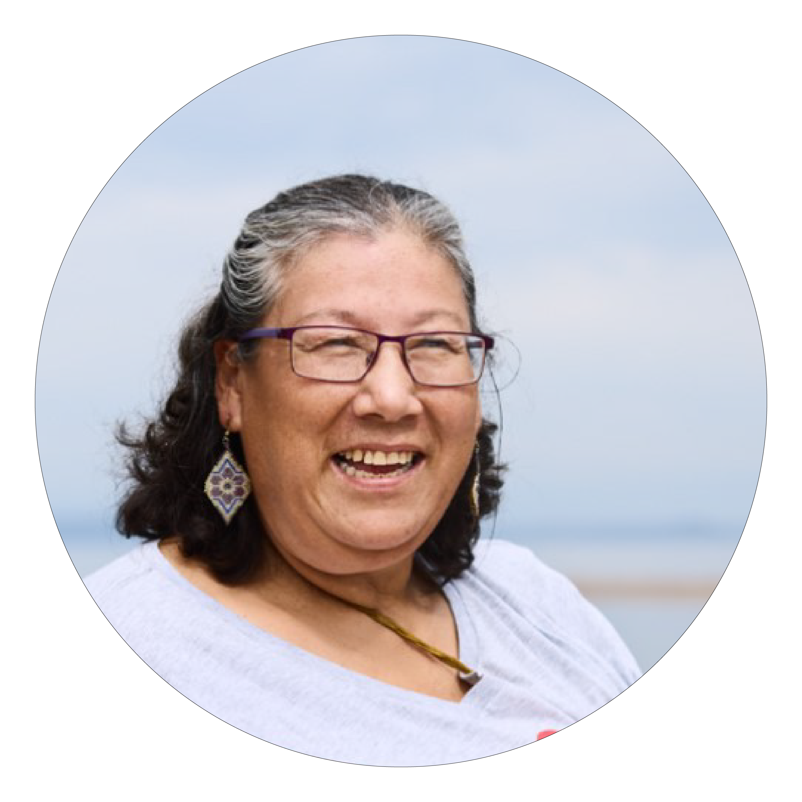 A woman with black and grey hair in a white shirt and glasses, smiling