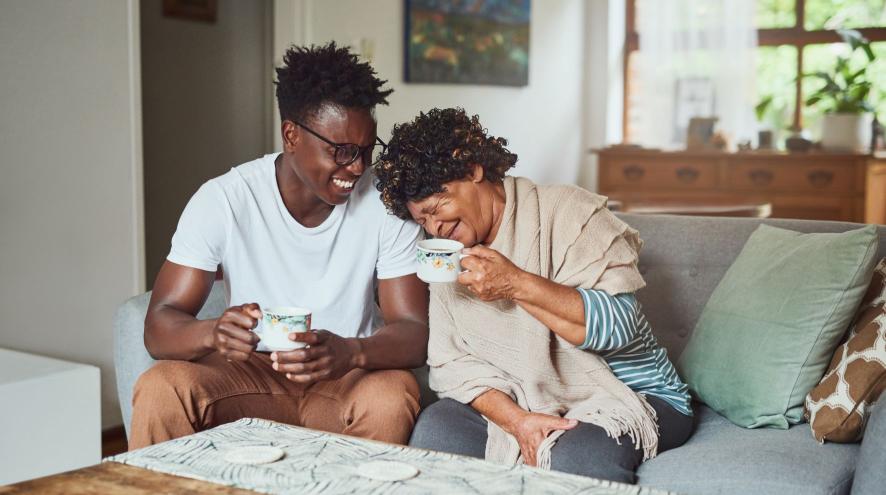 Younger man and older woman sit on couch having tea and conversation