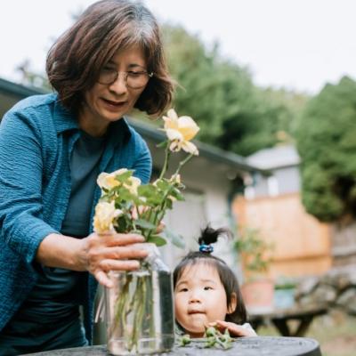 Senior woman putting flowers in a glass vase while her granddaughter watches.