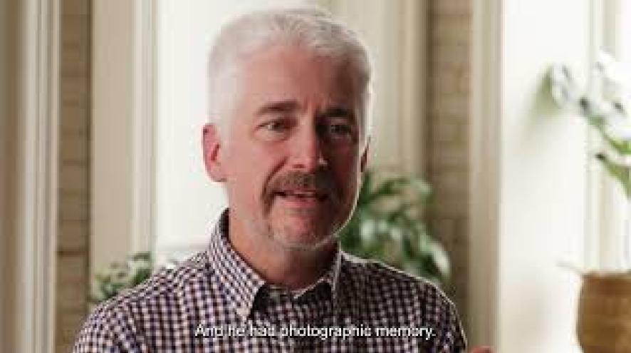 A midlife man speaking in an interior space