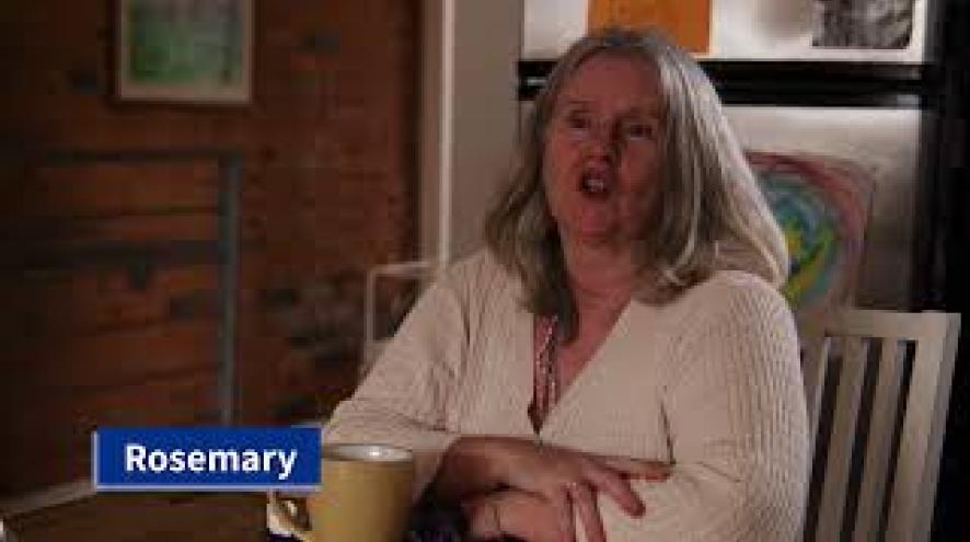 A midlife woman sits at a kitchen table, talking